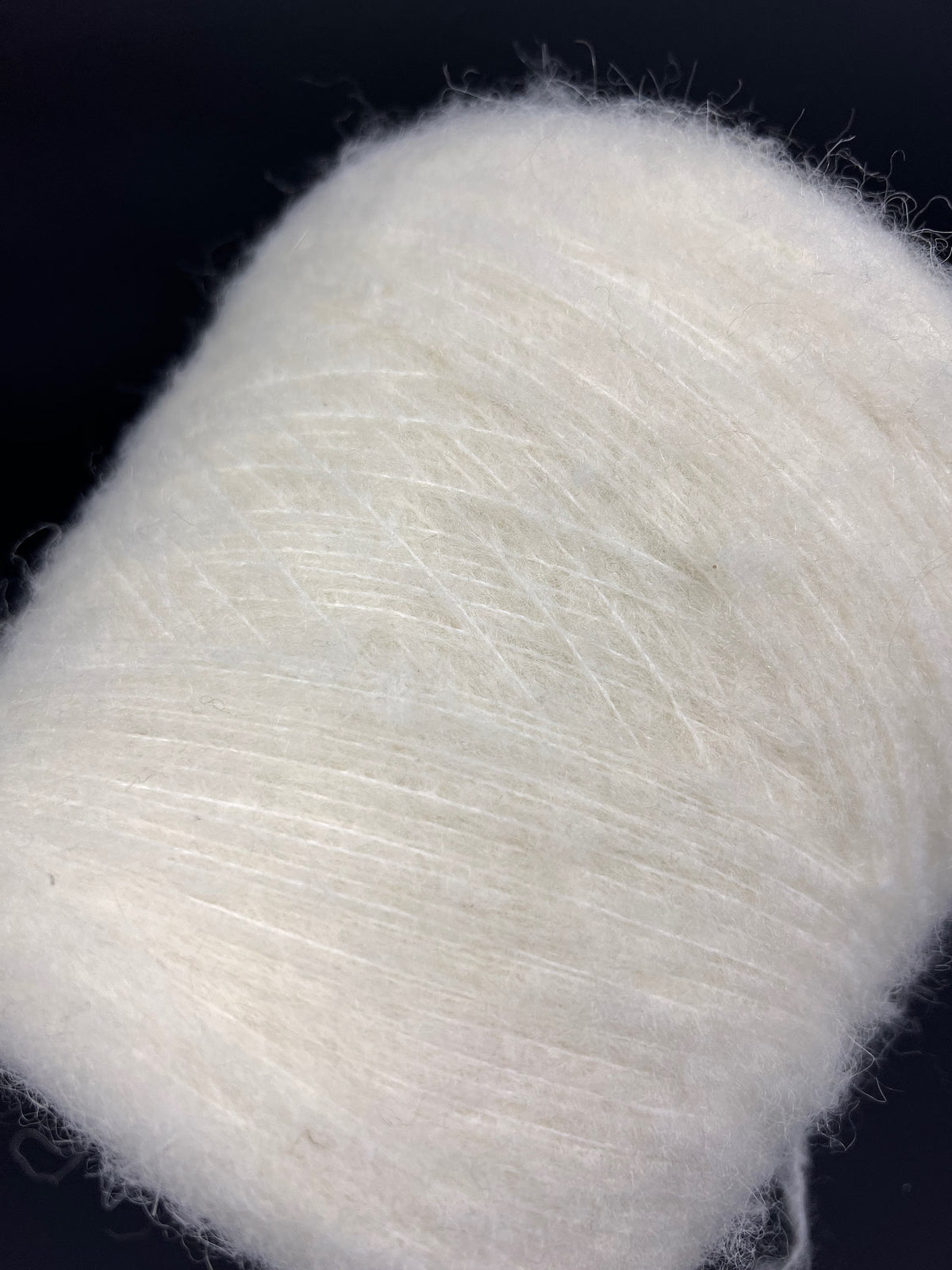 Close-up of a skein of un-dyed, naturally colored yarn. It has a slightly irregular texture with visible fine fibers and a soft, matte sheen, indicating a fluffy, gentle twist.