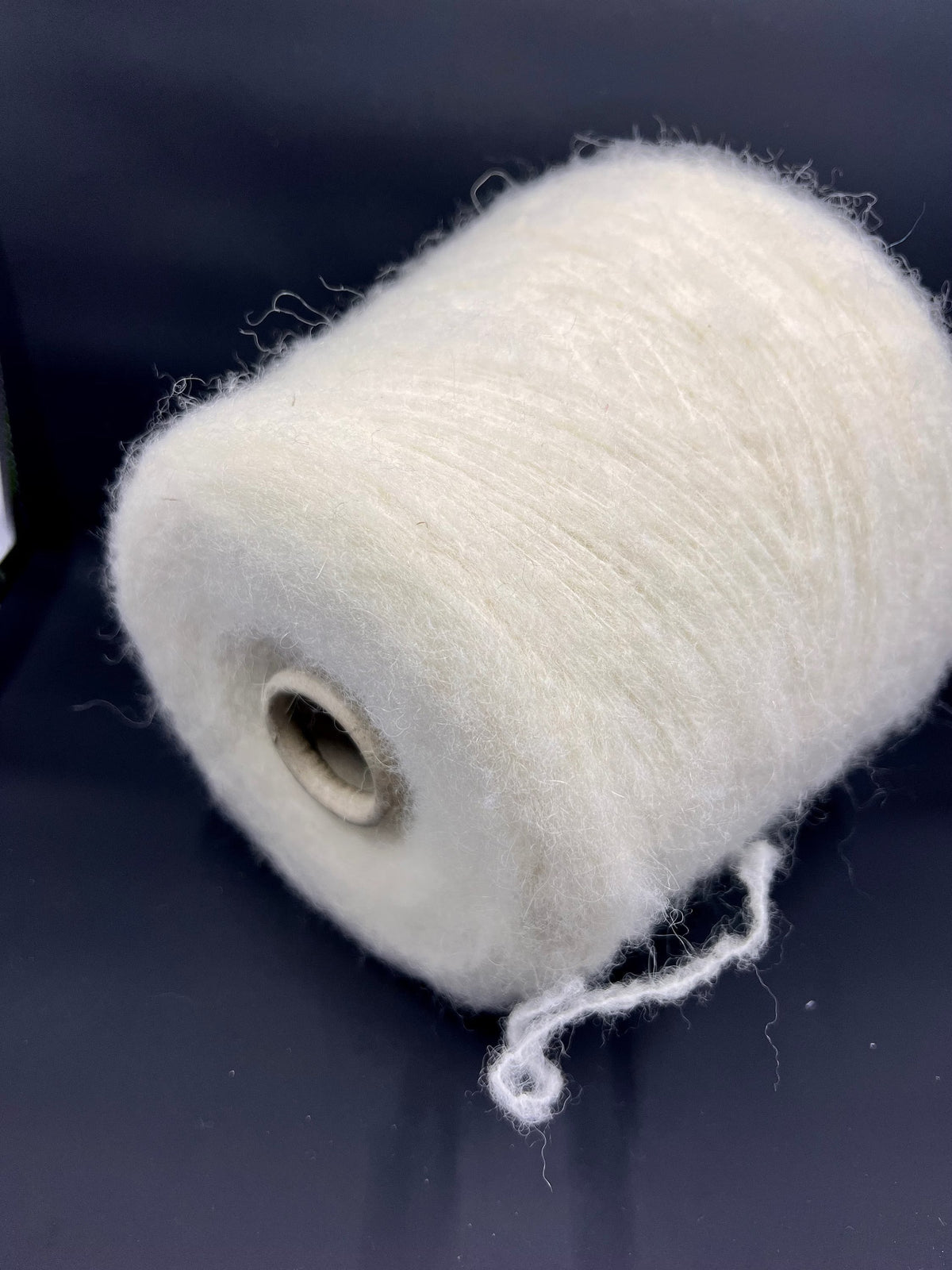 Close-up of a skein of un-dyed, naturally colored yarn. It has a slightly irregular texture with visible fine fibers and a soft, matte sheen, indicating a fluffy, gentle twist.
