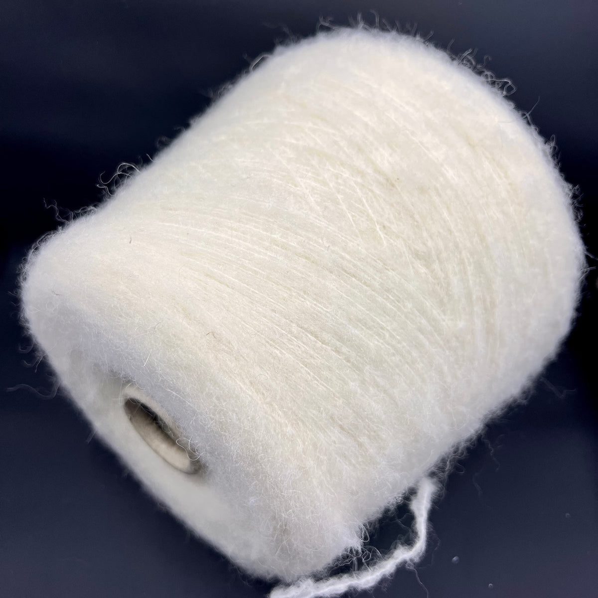 Close-up of a skein of un-dyed, naturally colored yarn. It has a slightly irregular texture with visible fine fibers and a soft, matte sheen, indicating a fluffy, gentle twist.