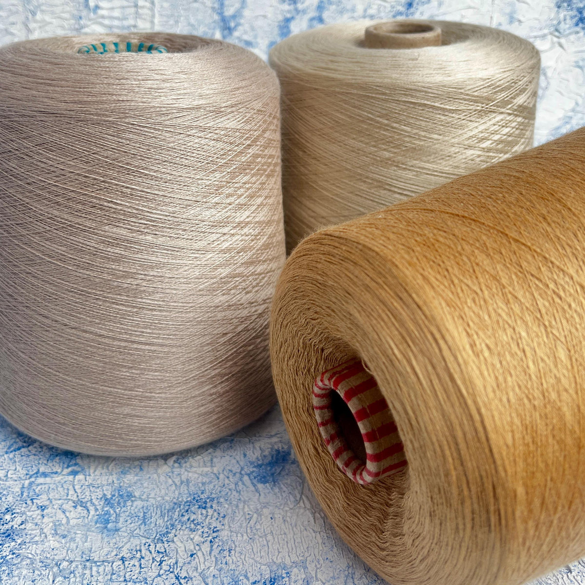 Smooth beige yarn, subtly twisted into a lustrous strand, wound neatly on a cylindrical cone, reflecting a delicate, soft sheen.