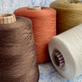 Close-up of a neatly wound cone of light brown, warm Cotto colored yarn with a subtle, elegant sheen, showcasing its fine, smooth plies.