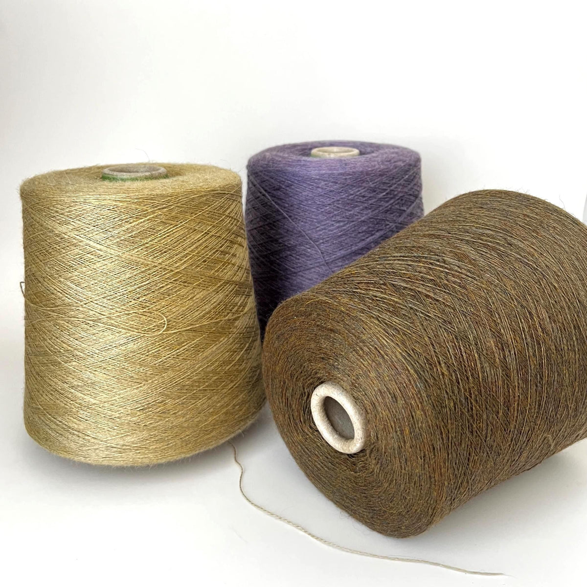 Close-up of a soft, fine two-ply yarn in a warm, muted straw-gold melange hue, showing a delicate halo and subtle sheen.