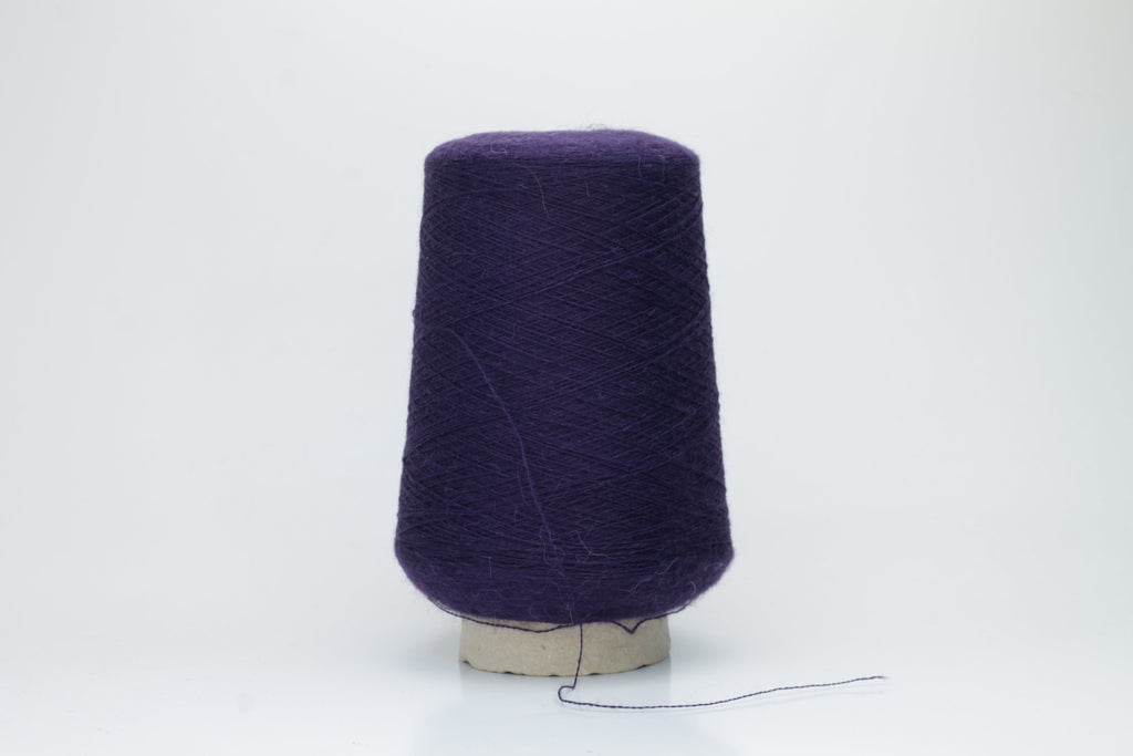 Close-up of a skein of rich, deep plum-toned yarn with a soft, ethereal halo, revealing a finely twisted thread structure and subtle sheen.