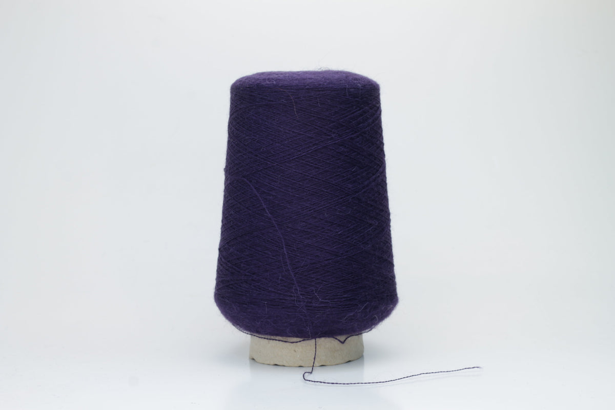 Close-up of a skein of rich, deep plum-toned yarn with a soft, ethereal halo, revealing a finely twisted thread structure and subtle sheen.