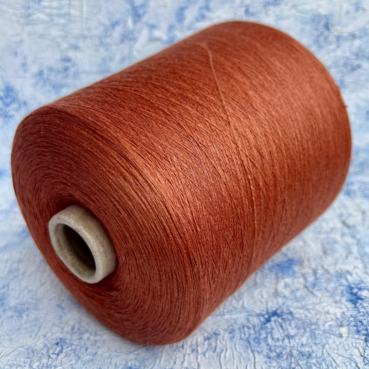 Close-up of a neatly wound cone of light brown, warm Cotto colored yarn with a subtle, elegant sheen, showcasing its fine, smooth plies.