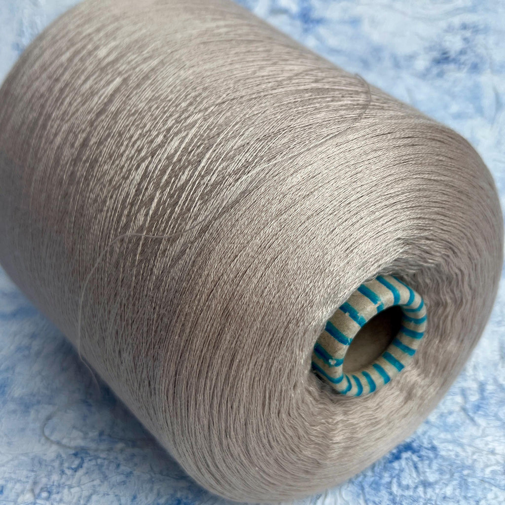 Smooth beige yarn, subtly twisted into a lustrous strand, wound neatly on a cylindrical cone, reflecting a delicate, soft sheen.