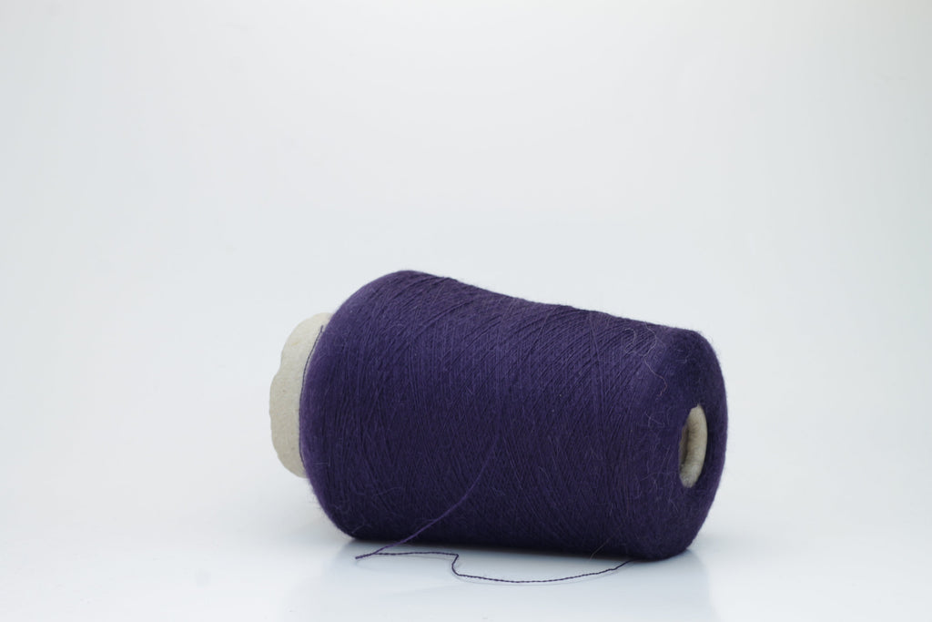 Close-up of a skein of rich, deep plum-toned yarn with a soft, ethereal halo, revealing a finely twisted thread structure and subtle sheen.