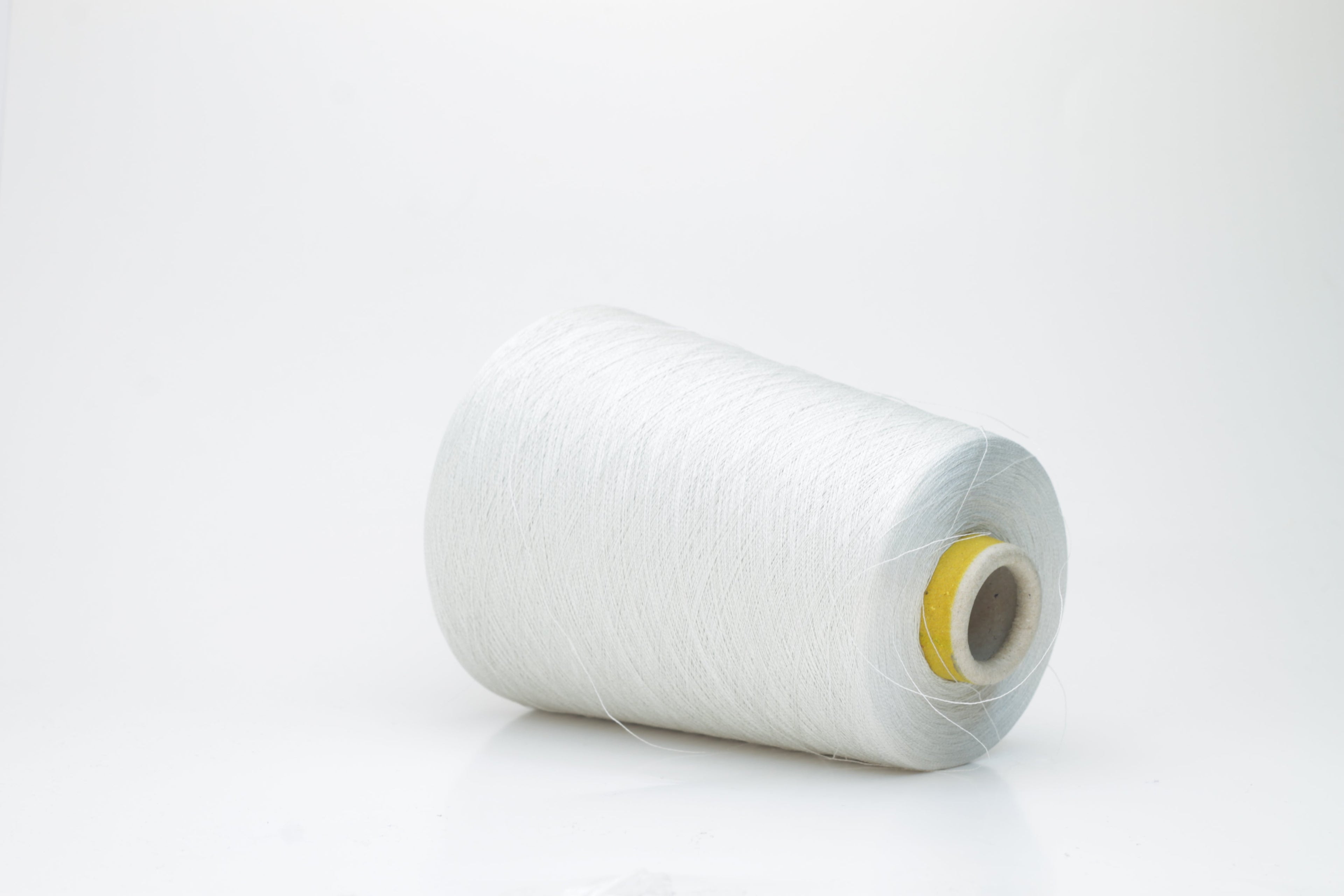Coiled skein of finely spun, two-ply light gray yarn with a subtle, cool metallic sheen, demonstrating a smooth, uniform twist and refined texture.