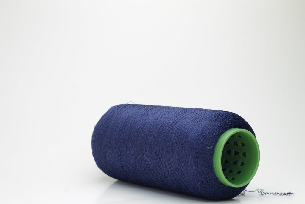 A tightly twisted, smooth two-ply thread of deep indigo blue, glistening with a high-luster sheen, wound onto a symmetrical cone.
