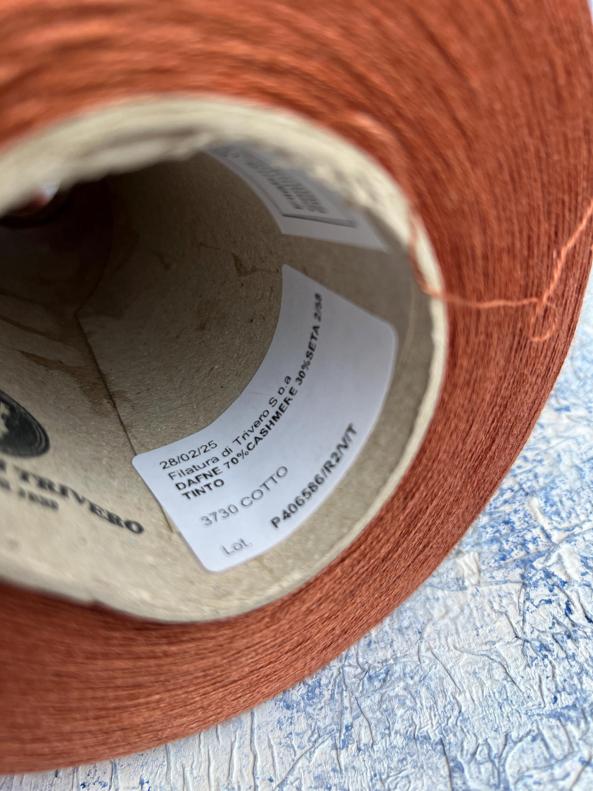 Close-up of a neatly wound cone of light brown, warm Cotto colored yarn with a subtle, elegant sheen, showcasing its fine, smooth plies.