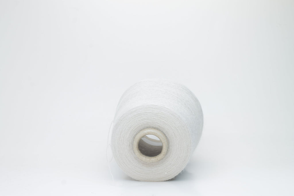A close-up of soft, matte beige yarn, meticulously twisted into a fine 2-ply strand, showcasing its subtle fluffiness and consistent texture. The natural, warm hue is uniform throughout.