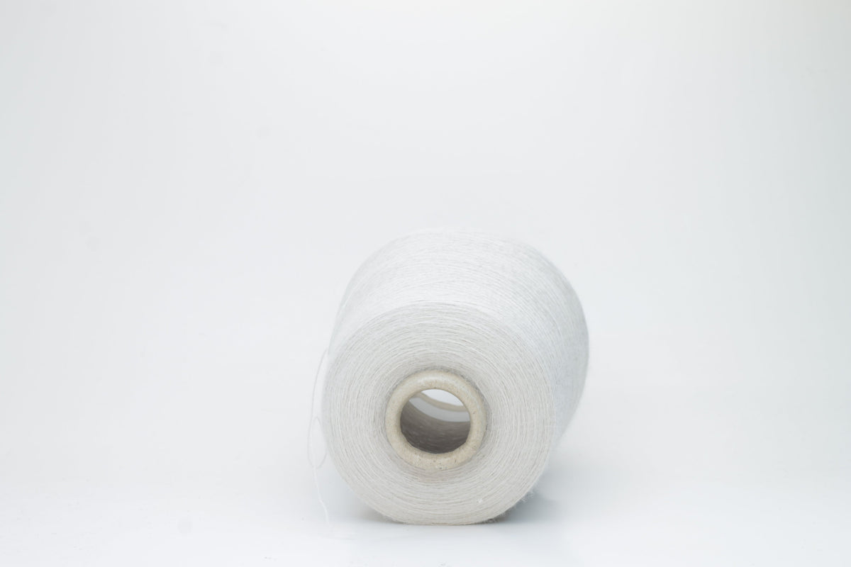 A close-up of soft, matte beige yarn, meticulously twisted into a fine 2-ply strand, showcasing its subtle fluffiness and consistent texture. The natural, warm hue is uniform throughout.