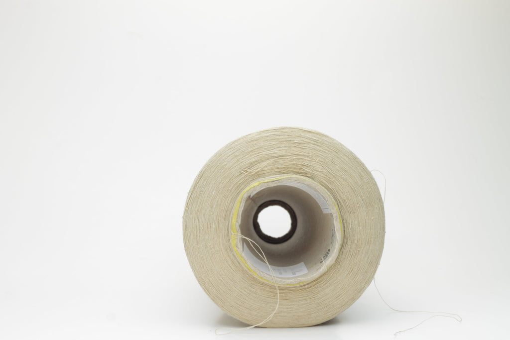 A skein of light beige yarn, showcasing a subtle sheen from the silk and a slight irregular texture from the linen fibers. The individual plies are gently twisted, creating a fluid, soft drape.
