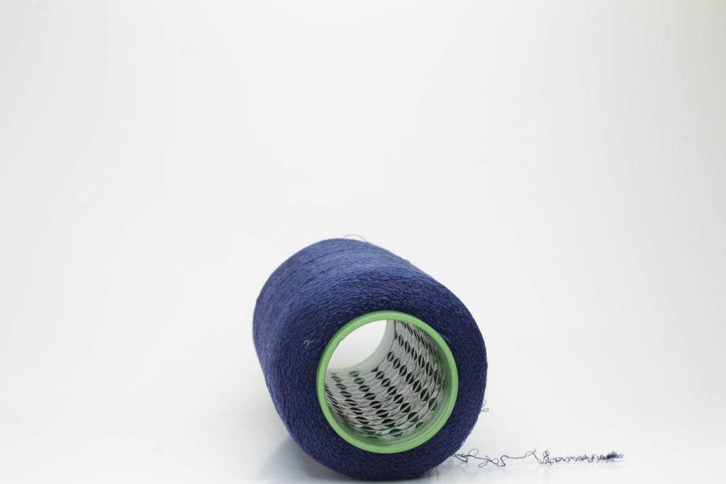 A tightly twisted, smooth two-ply thread of deep indigo blue, glistening with a high-luster sheen, wound onto a symmetrical cone.
