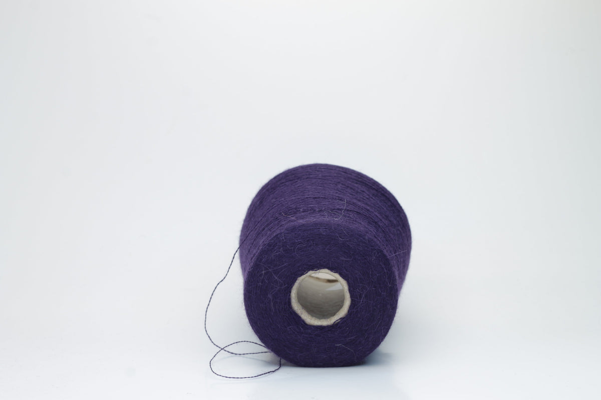 Close-up of a skein of rich, deep plum-toned yarn with a soft, ethereal halo, revealing a finely twisted thread structure and subtle sheen.