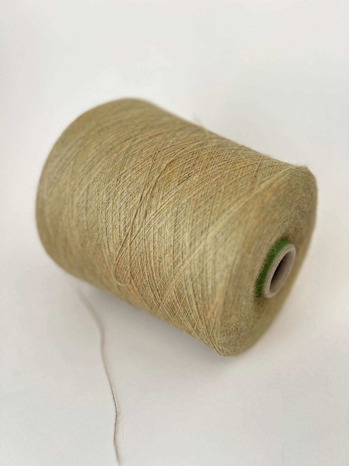 Close-up of a soft, fine two-ply yarn in a warm, muted straw-gold melange hue, showing a delicate halo and subtle sheen.