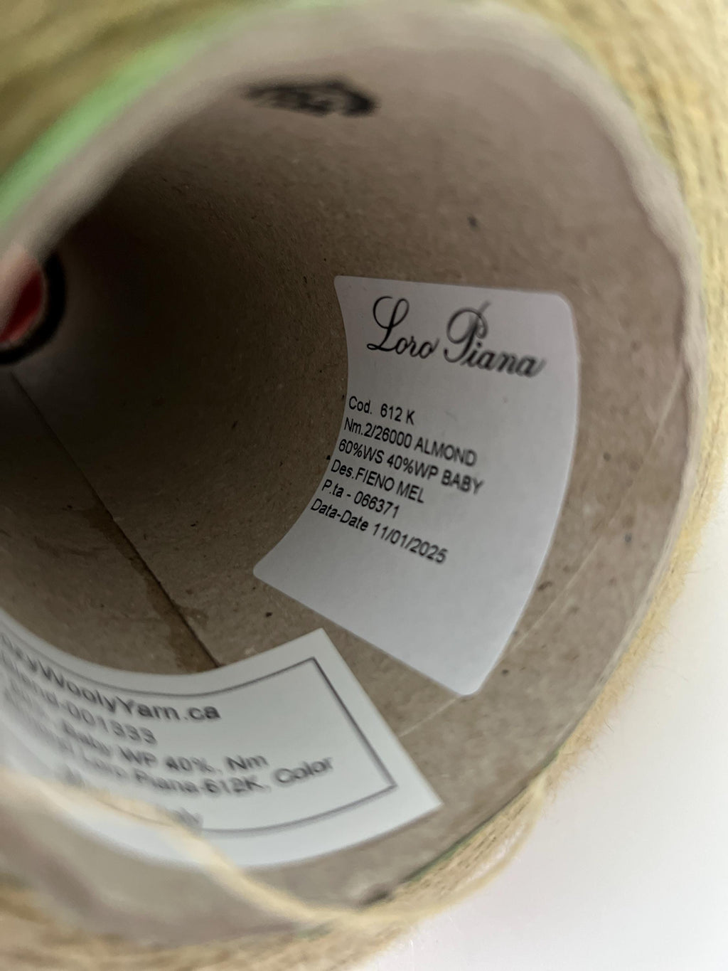 Close-up of a soft, fine two-ply yarn in a warm, muted straw-gold melange hue, showing a delicate halo and subtle sheen.